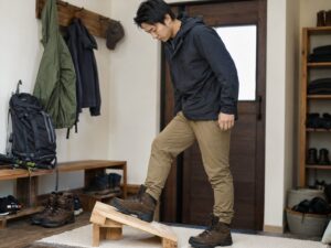 自宅の玄関で傾斜板を使い、新品登山靴のフィット感を確認する男性ハイカー