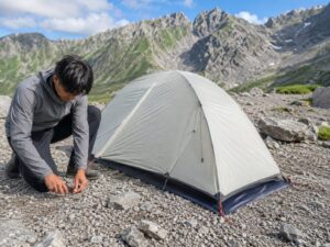 岩場のテント場でペグを打ち、山岳テントを設営する登山者