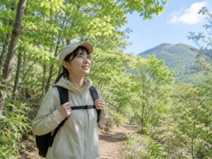 晴れた低山の登山道を歩く薄手レインウェアの女性