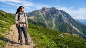 登山道でストックを持つ日本人女性ハイカーが、山のルートを見ながら必要性を判断している様子