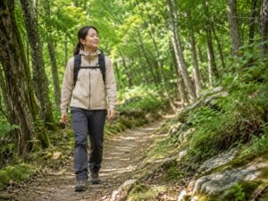 ストックなしで森の登山道を歩く日本人女性ハイカーの様子