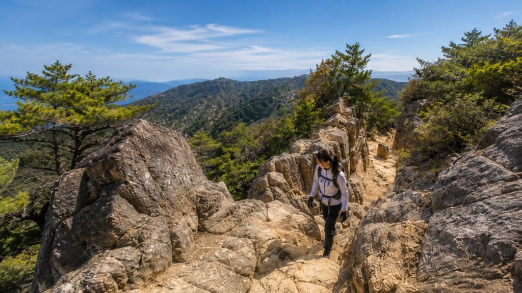 六甲山の岩場が続く登山ルートを慎重に歩く女性ハイカー