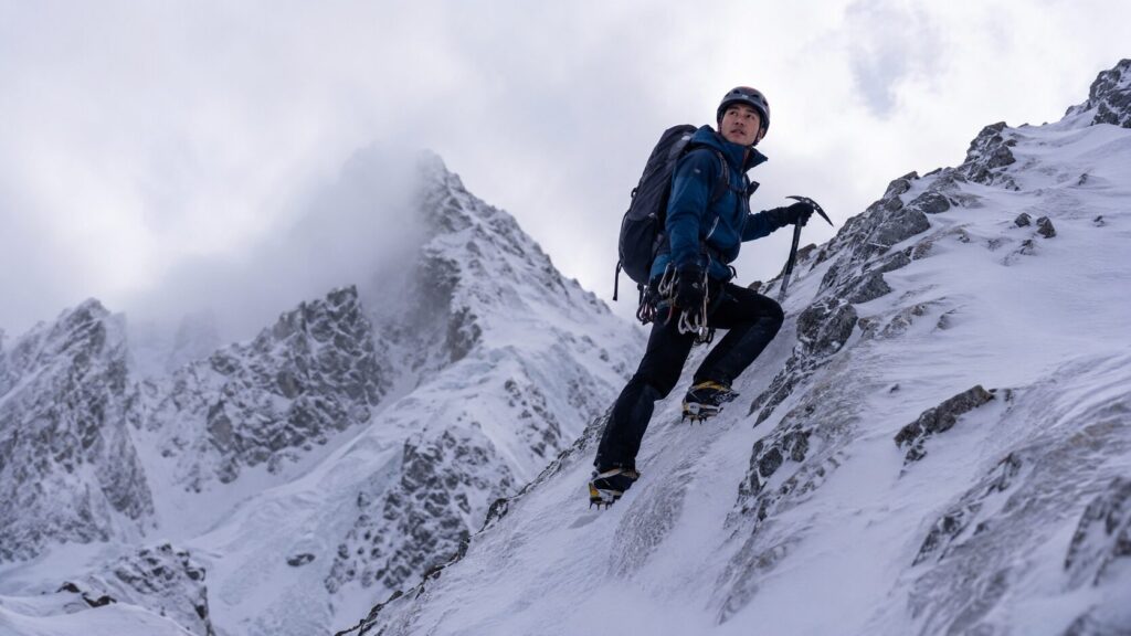 ピッケルとアイゼンを使用して急な雪山を登る日本人登山者